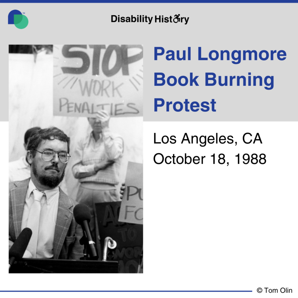 Black and white photo of Paul Longmore sitting in a wheelchair, wearing glasses and in front of a microphone. Behind him are fellow protesters and one holds a sign that says, “Stop work penalties.” Text: Paul Longmore Book Burning Protest. Los Angeles, CA. October 18, 1988. Source: Tom Olin. 