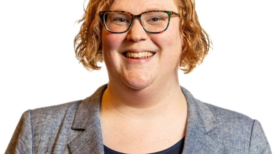 Ariel Simms smiling headshot wearing a grey blazer and a black shirt