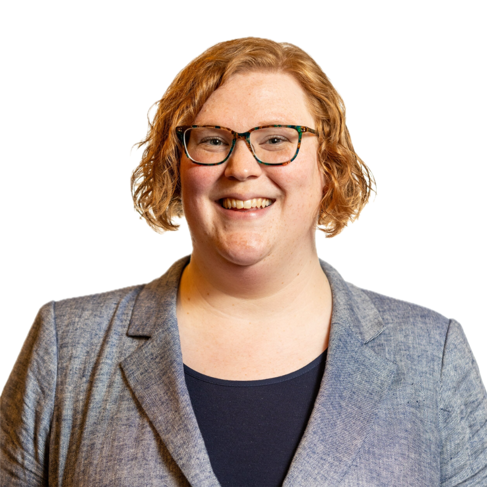 Ariel Simms smiling headshot wearing a grey blazer and a black shirt