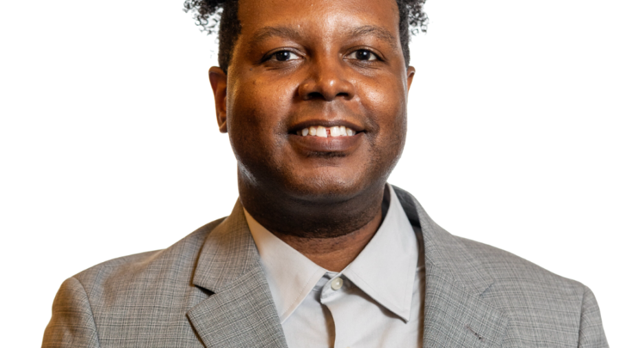 Graciano Petersen smiling headshot wearing a grey patterned blazer and a grey dress shirt