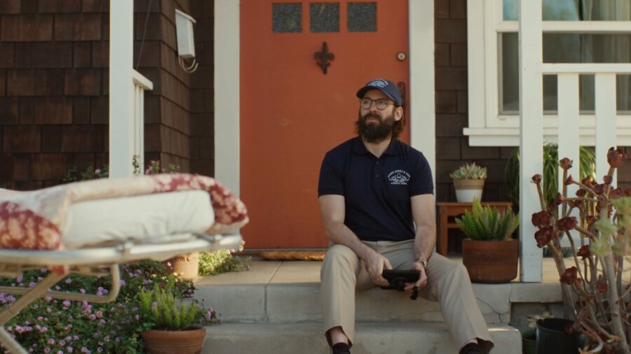 a scene from the short film Out For Delivery with a man seated outside a person's door with a hospital bed in front of him