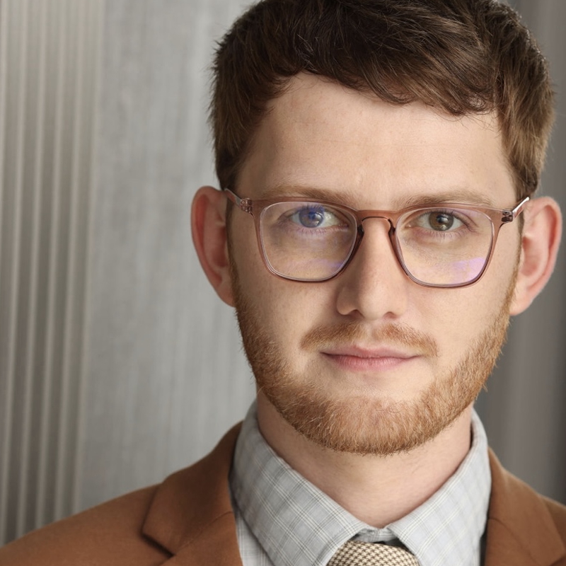 Aaron Potter smiling headshot wearing a brown suit and glasses