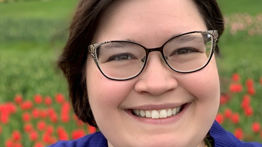 Gina DeRyke smiling headshot in front of flowers in the background