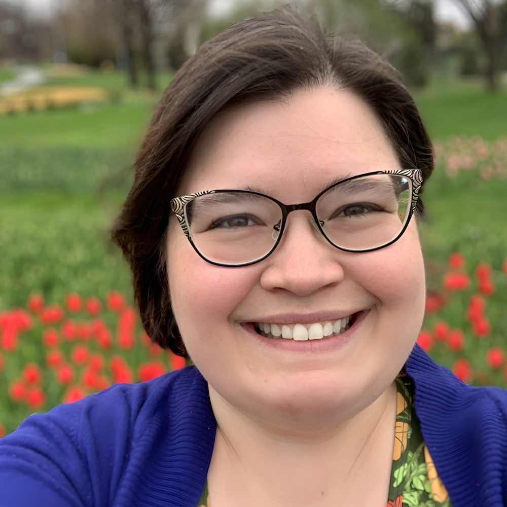 Gina DeRyke smiling headshot in front of flowers in the background