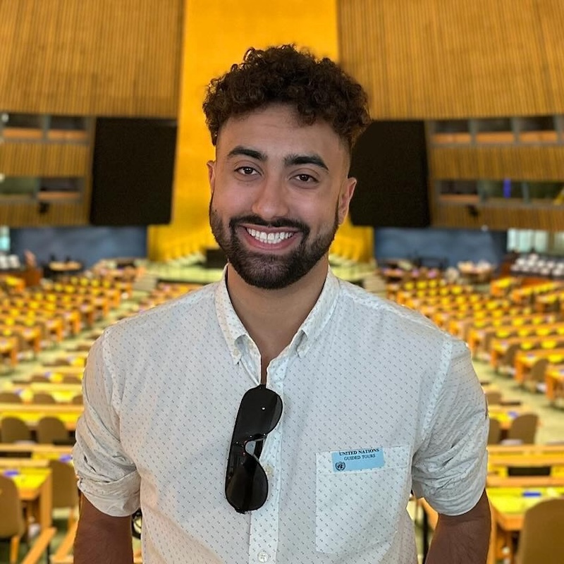 Miles Robinson smiling headshot in front of the United Nations General Assembly hall