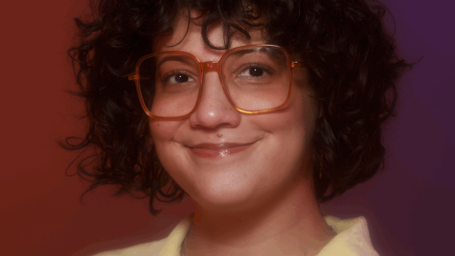 Ana Maria Defillo smiling headshot wearing a yellow polo and red glasses
