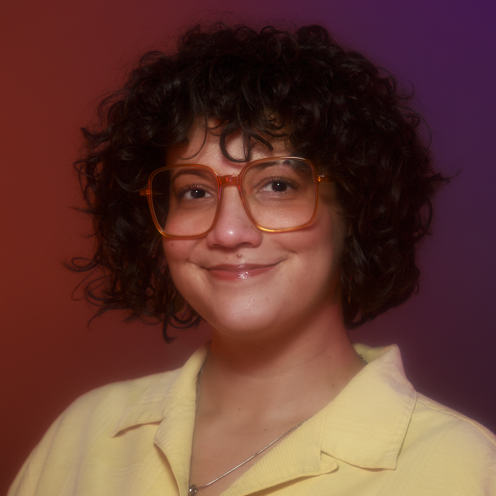 Ana Maria Defillo smiling headshot wearing a yellow polo and red glasses