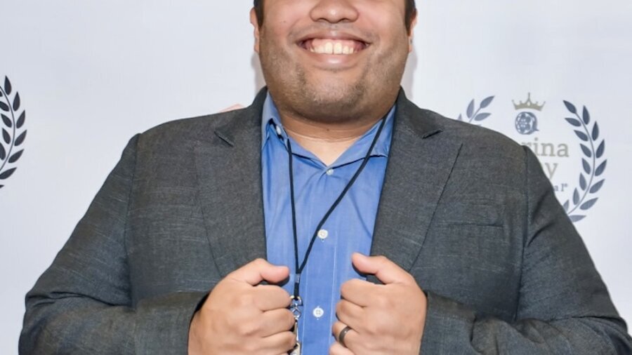Miguel Martinez smiling wearing a grey blazer in front of a step and repeat banner with the Regal logo on it