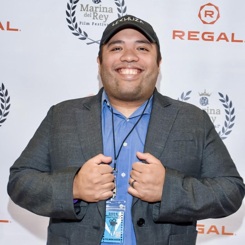 Miguel Martinez smiling wearing a grey blazer in front of a step and repeat banner with the Regal logo on it
