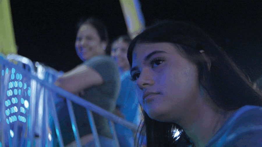 A woman with long, dark hair looks thoughtfully into the distance. In the background are two smiling women.