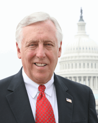 Congressman Steny Hoyer smiling wearing a suit and tie with the Capitol dome behind him